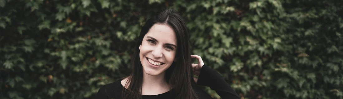 A woman smiling in front of greenery.